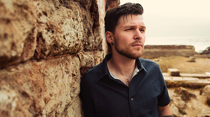 jayson angove leaning against a brown stone wall